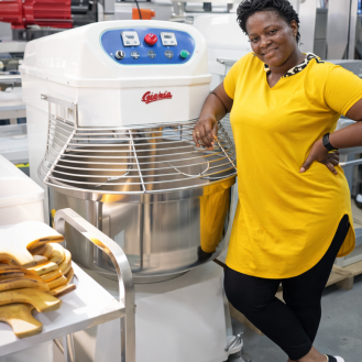 Woman stands next to bakery oven.