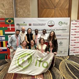 A group of people poses with an organisation's flag, in front of banners