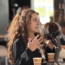 Holding a microphone, a woman asks a question animatedly.